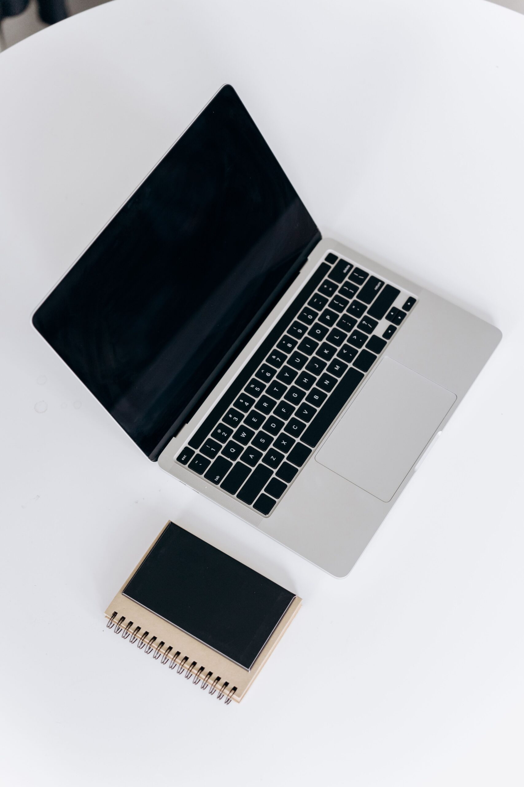 Overhead view of a sleek laptop and notebook on a white table, ideal for a minimalist workspace.